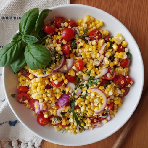 Fresh summer corn salad with tomatoes red onion and basil in a serving bowl
