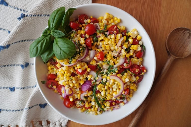 Fresh summer corn salad with tomatoes red onion and basil in a serving bowl
