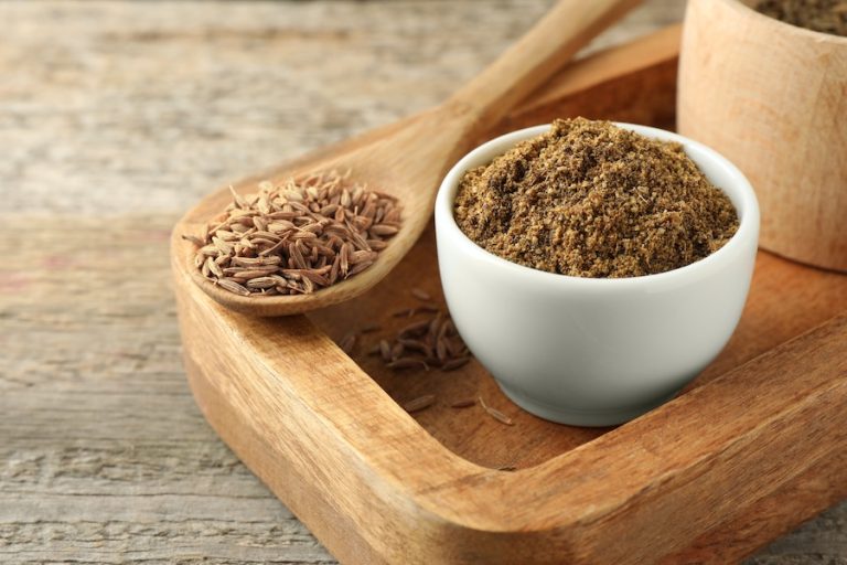 Ground cumin and cumin seeds displayed in bowls and wooden spoons