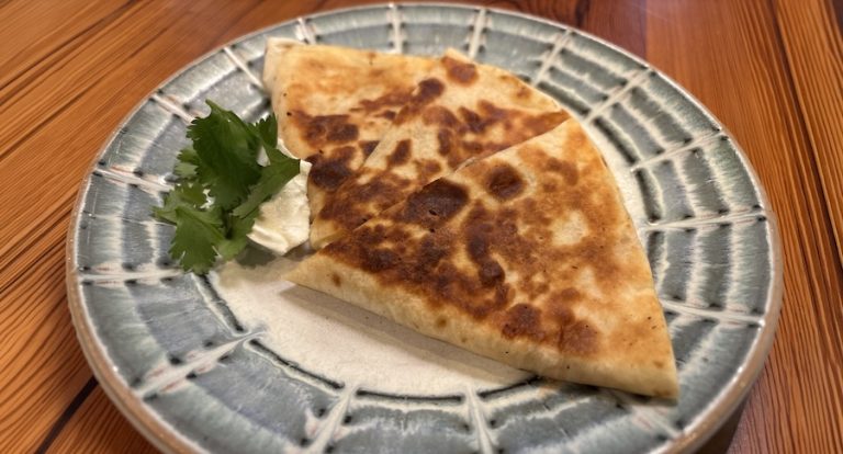 Golden brown sage sausage and chèvre quesadilla served with fresh salsa on a ceramic plate.
