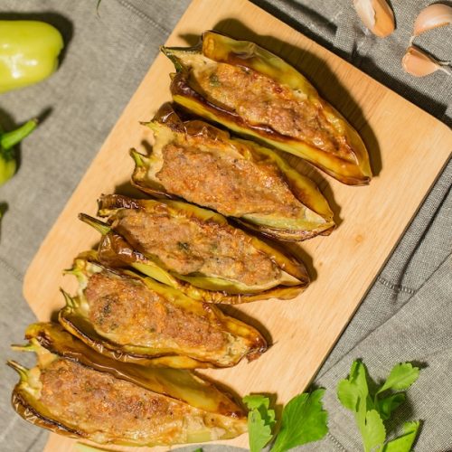 Fresh banana peppers and pork-stuffed banana peppers served on a wooden cutting board.