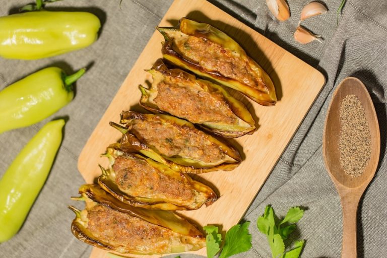 Fresh banana peppers and pork-stuffed banana peppers served on a wooden cutting board.