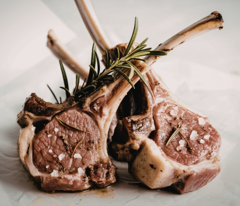 Three succulent lamb chops, seasoned with salt and rosemary, are artfully arranged on parchment paper. The image showcases their rich, browned exterior and juicy interior.