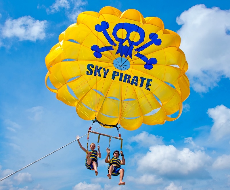 Two friends parasailing above Hilton Head Island with panoramic coastal views.