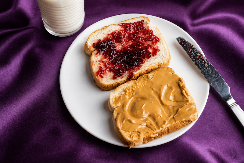 Peanut butter and jelly sandwich being made on a purple table cloth