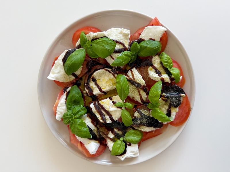 Homemade Caprese salad made from mozzarella cheese, fresh tomatoes, fresh basil, olive oil and balsamic vinegar on a plate directly above view