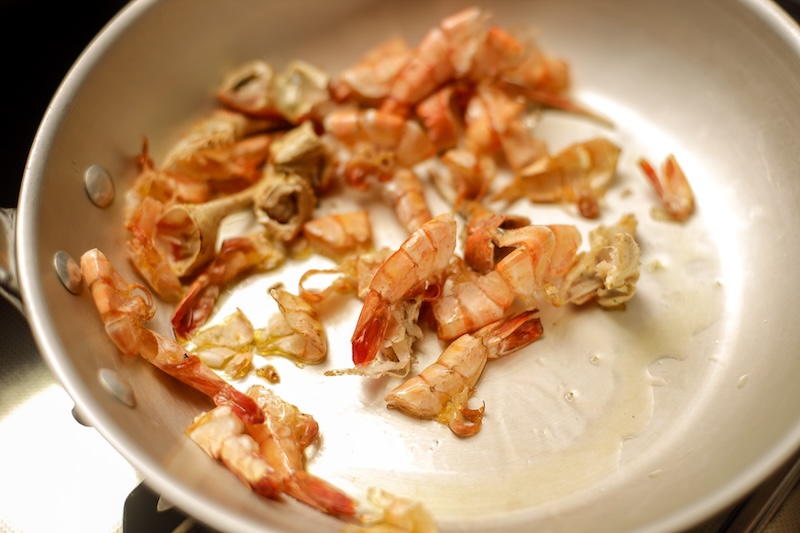 Shrimp shells sautéing in a saucepan to build flavor for homemade shrimp stock.