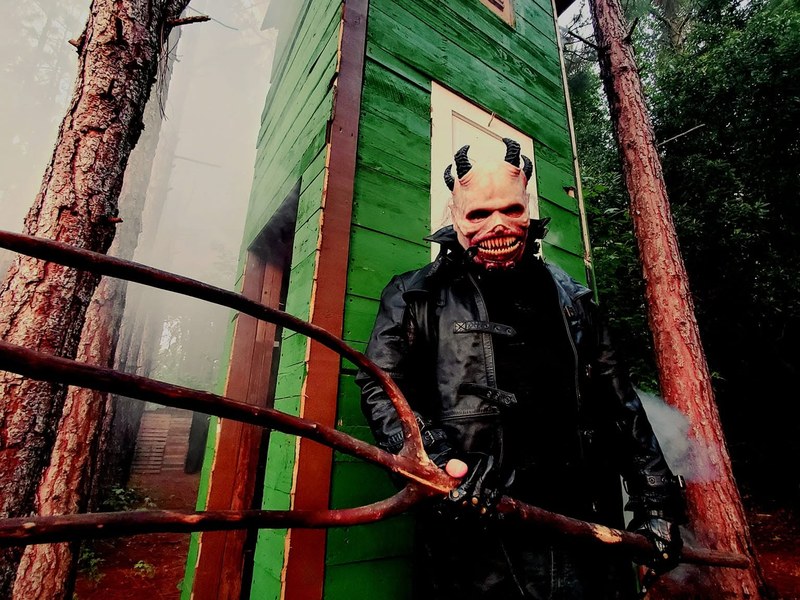 Masked character emerging from a doorway in a wooded setting
