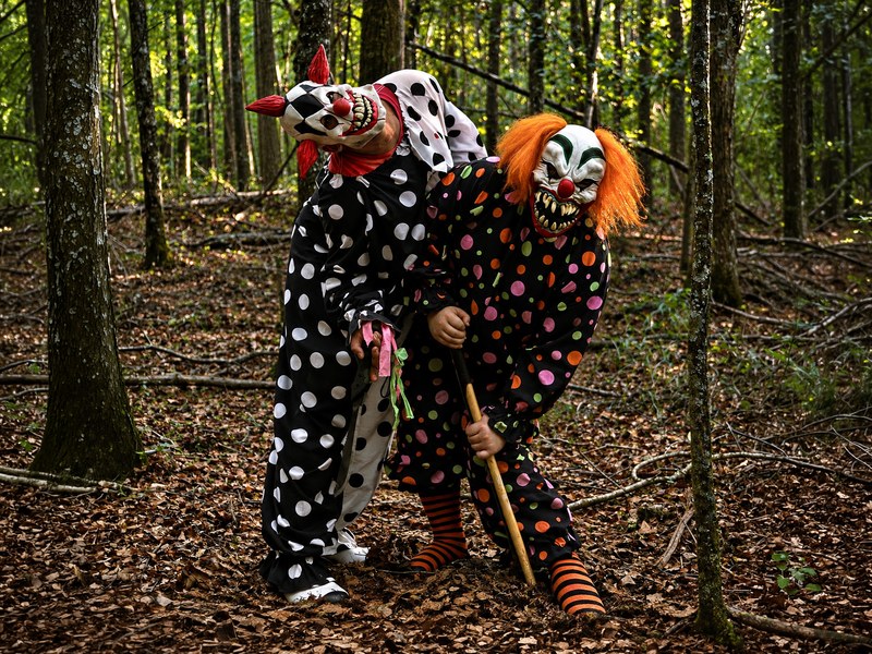 Two costumed clowns standing on a wooded trail