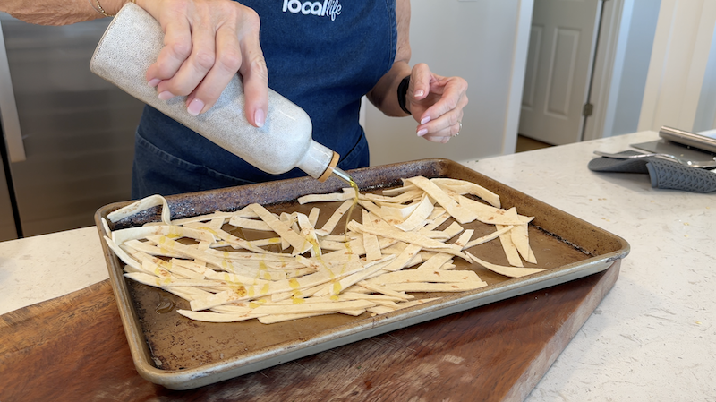 Tortilla strips on a baking sheet being seasoned before baking