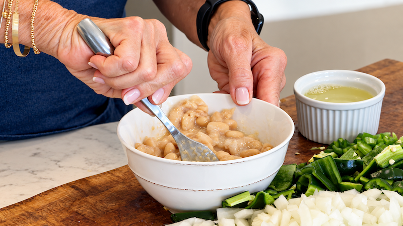 White beans being mashed with a fork to create a creamy chili base