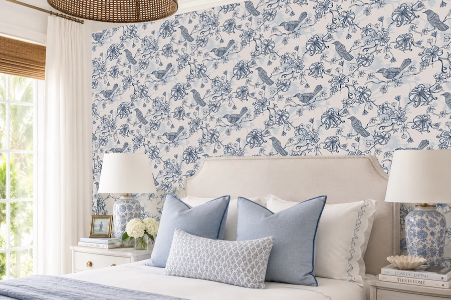 Bedroom with blue-and-white botanical wallpaper behind an upholstered bed with blue accent pillows