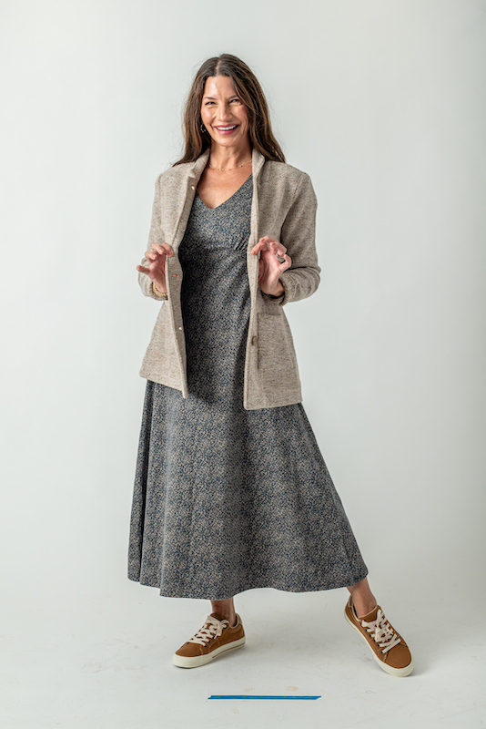 Woman wearing a tan knit jacket over a dark blue floral dress with brown sneakers