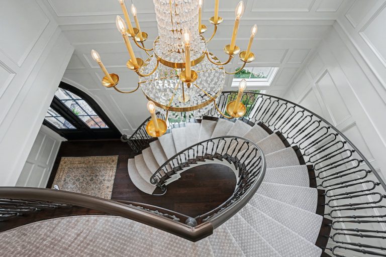 View from above of a curved staircase beneath a crystal chandelier in a white paneled foyer