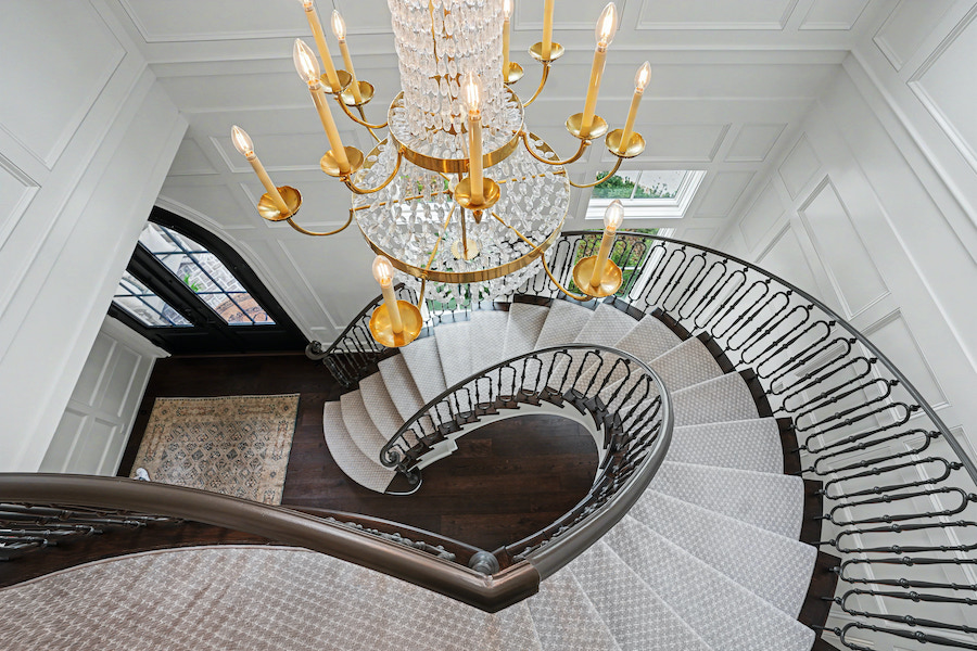 View from above of a curved staircase beneath a crystal chandelier in a white paneled foyer