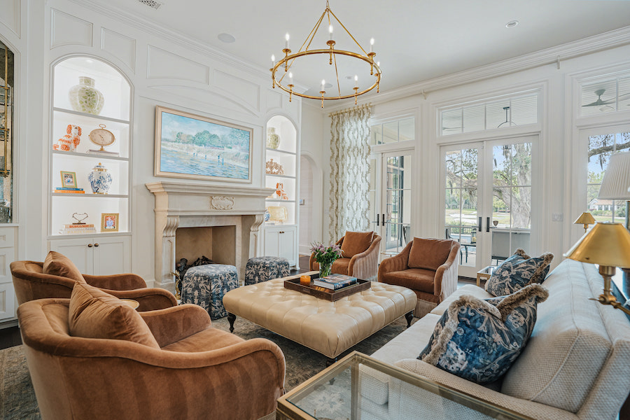 Light-filled living room with arched built-in cabinets, fireplace, warm brown armchairs and a tufted ottoman