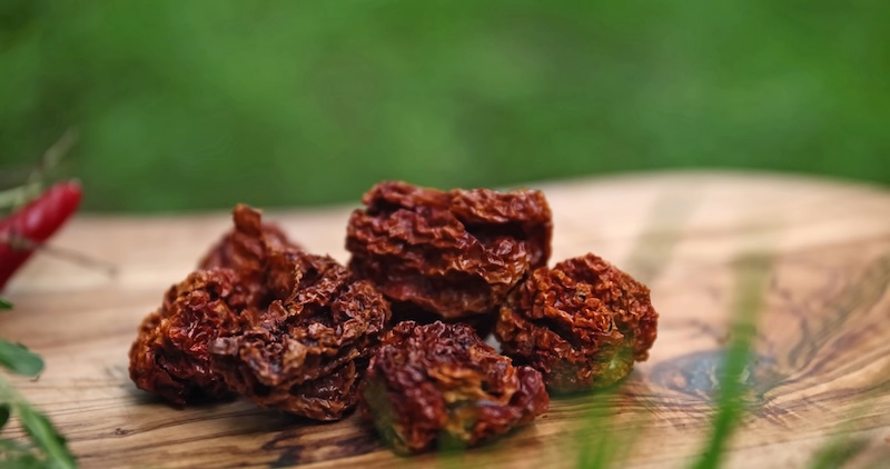 Several dried, wrinkled red Carolina Reaper peppers arranged on a wooden surface.