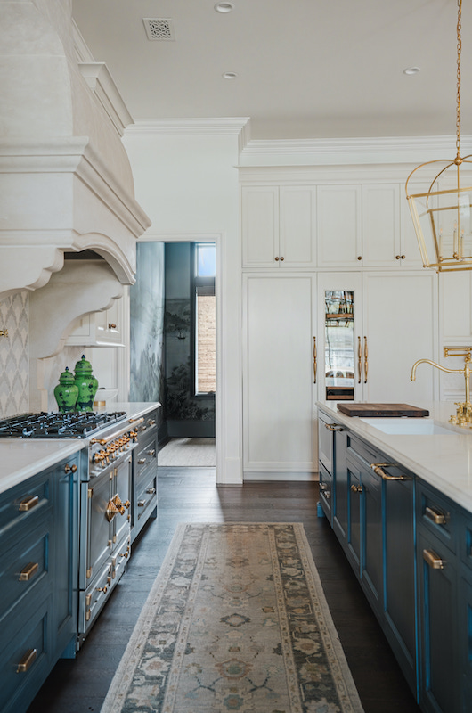 Bright kitchen with creamy white cabinetry, blue island cabinetry and brass pendant lights