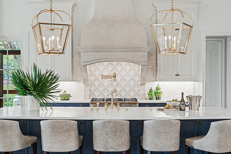 Bright kitchen with creamy white cabinetry, blue island cabinetry and brass pendant lights and island