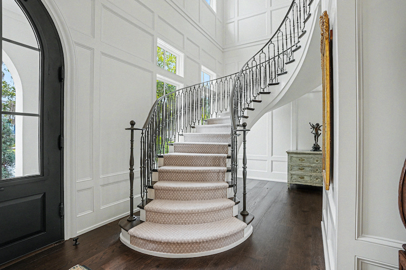 Curved staircase with an intricate dark railing rising through a paneled foyer