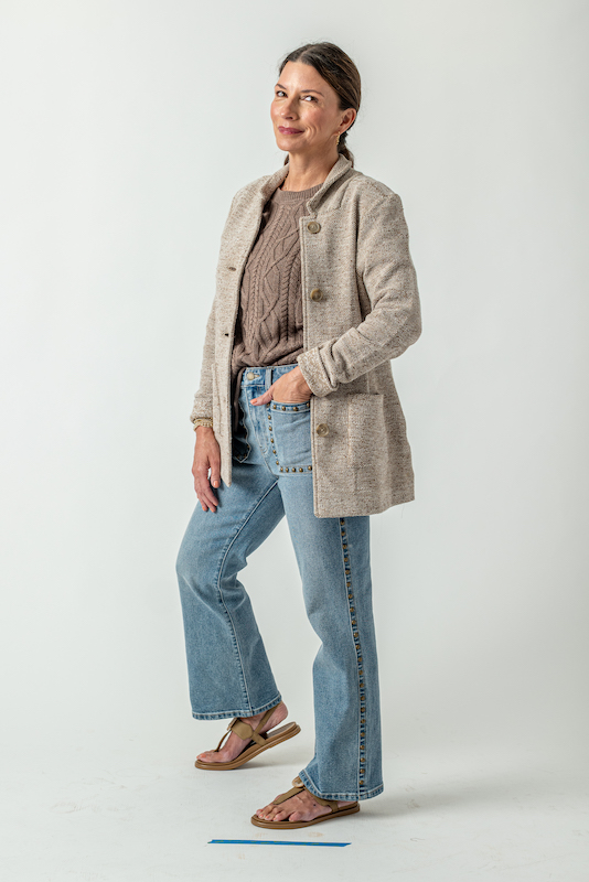Woman wearing a tan knit jacket with a neutral sweater, statement jeans and tan sandals