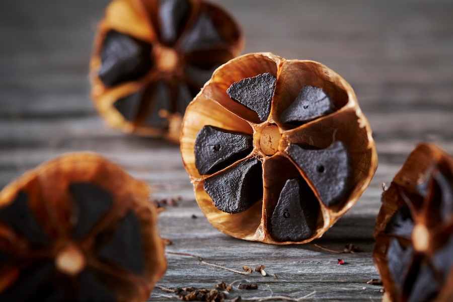 Black garlic bulbs cut open to reveal dark aged cloves