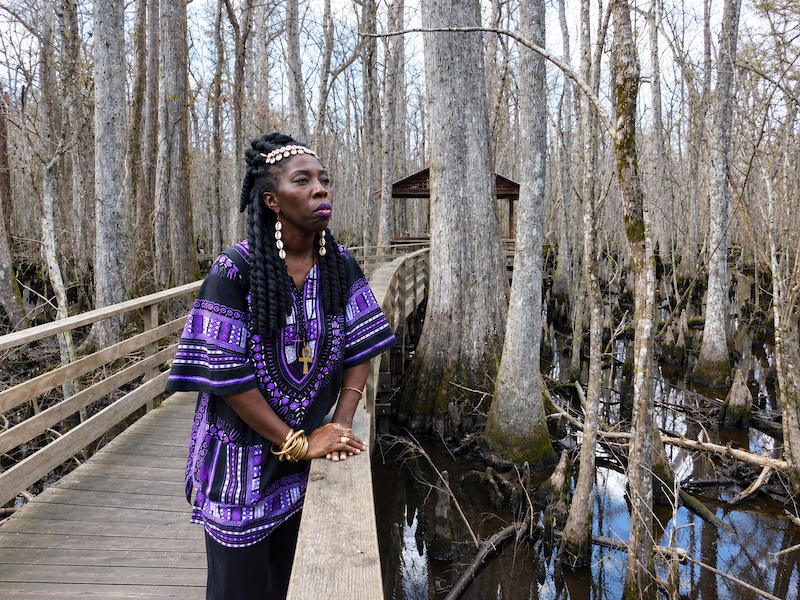 Queen Quet standing on a wooden walkway surrounded by trees