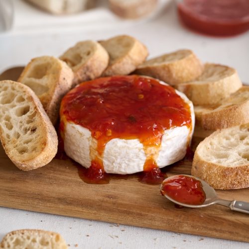 Round cheese topped with red pepper jelly and surrounded by toasted bread slices.