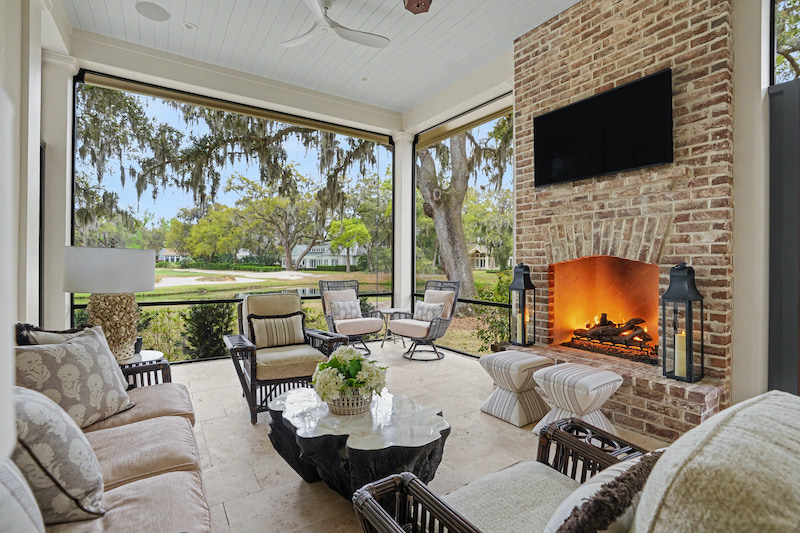 Screened porch with brick fireplace, television and neutral lounge seating overlooking the outdoors