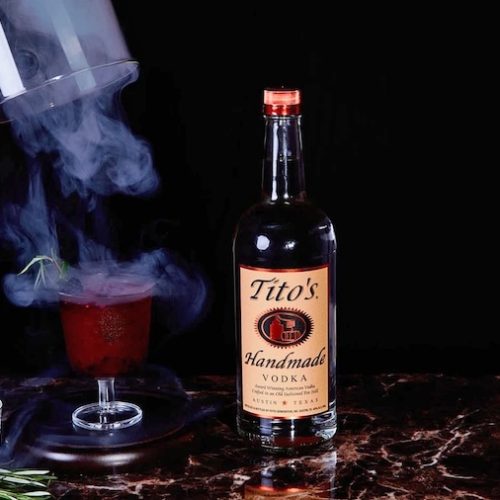 Red cocktail garnished with rosemary and blackberry surrounded by smoke