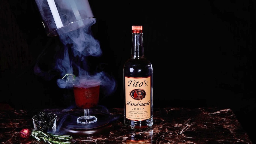 Red cocktail garnished with rosemary and blackberry surrounded by smoke
