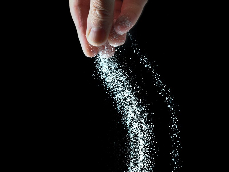 Hand sprinkling salt against a dark background