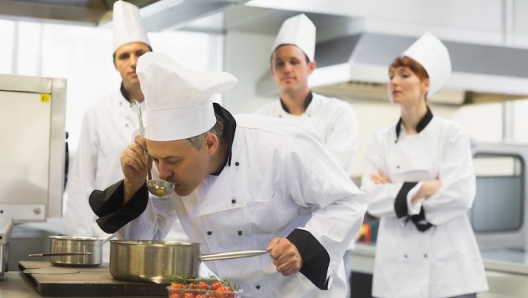 Chef cooking at a stove with other kitchen staff