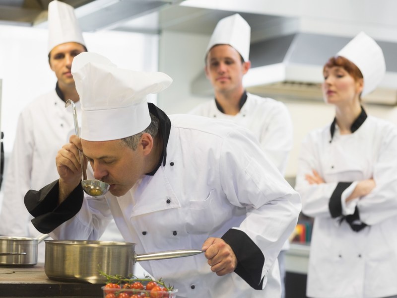 Chef cooking at a stove with other kitchen staff in the background