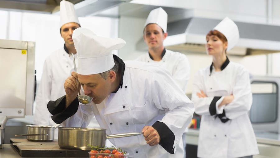 Chef cooking at a stove with other kitchen staff