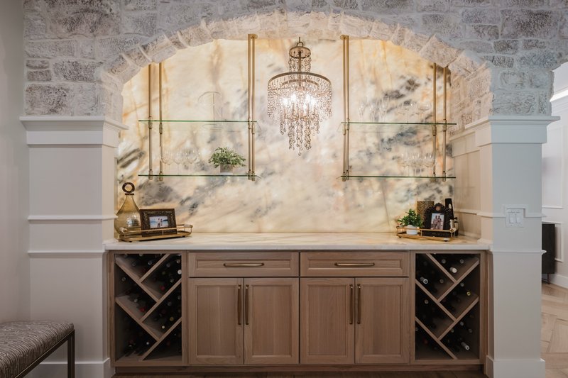 Custom wet bar with limestone arch, wine storage, cabinetry and chandelier