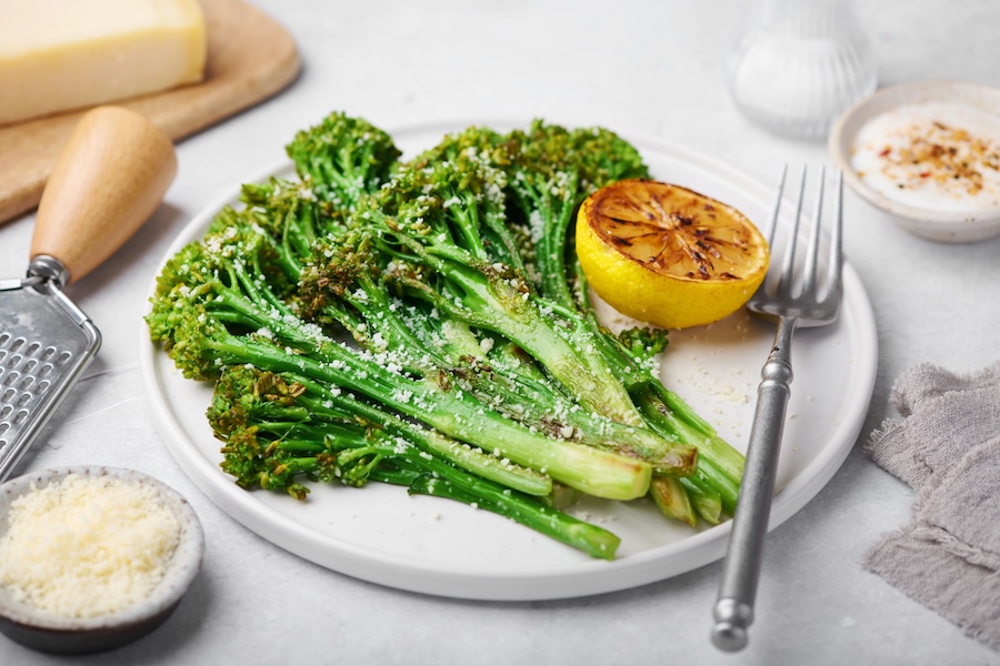 Fresh broccolini stalks with small green florets arranged on a dark wooden tabletop.
