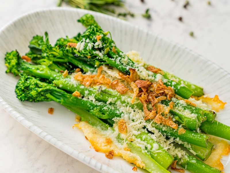 Roasted broccolini with a crisp golden topping served on an oval white platter.