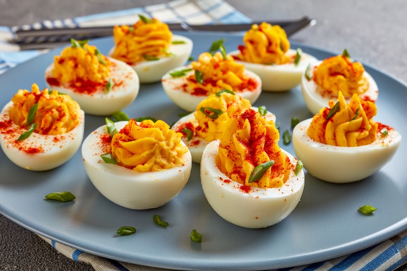 Deviled eggs with piped orange-yellow filling and colorful garnishes.