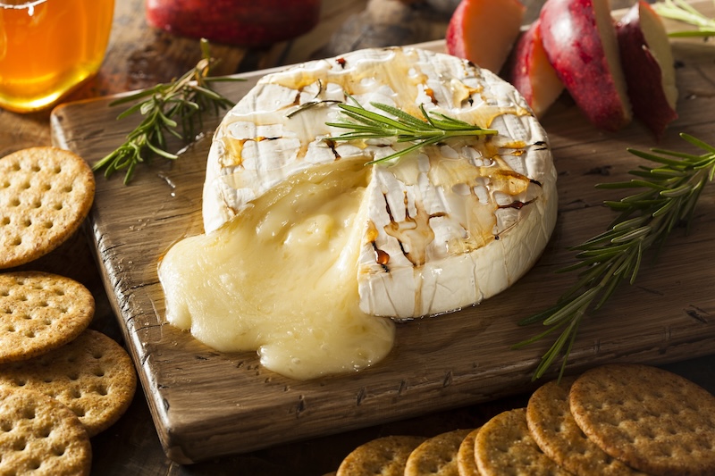 Warm baked brie with melted cheese flowing from the center, served with crackers and fruit.