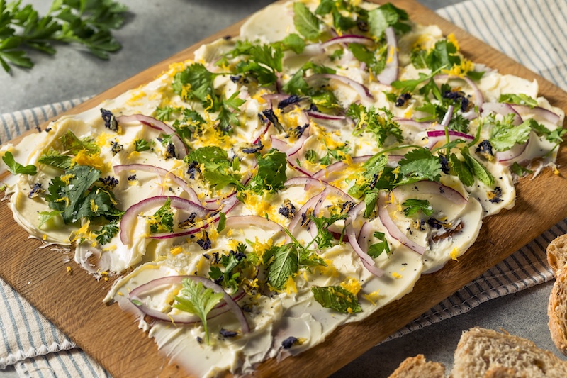 Spread of softened butter topped with herbs and seasonings on a serving board.