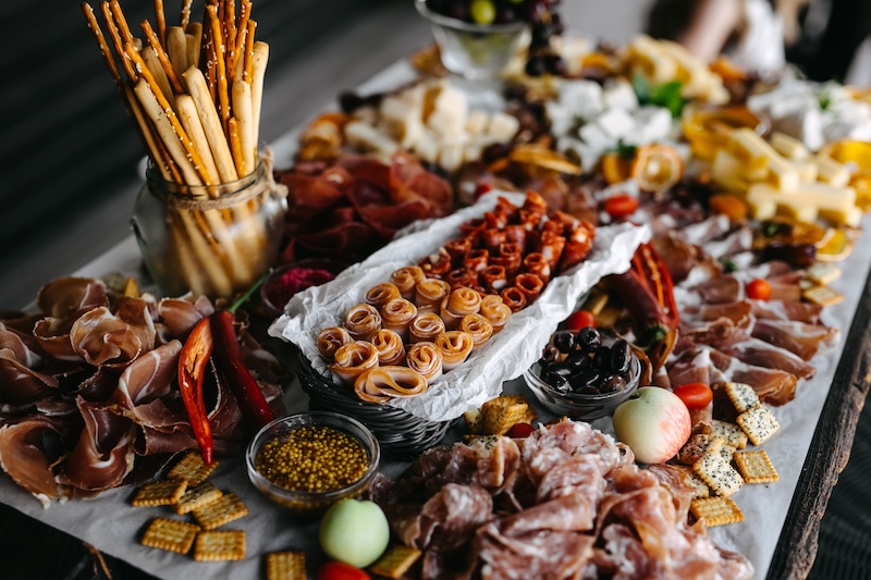Large charcuterie board arranged with cured meats, cheeses, breadsticks and accompaniments.