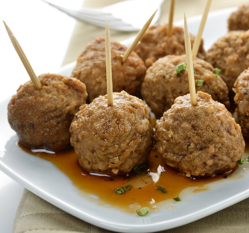 Cocktail meatballs with toothpicks served in sauce on a white platter.