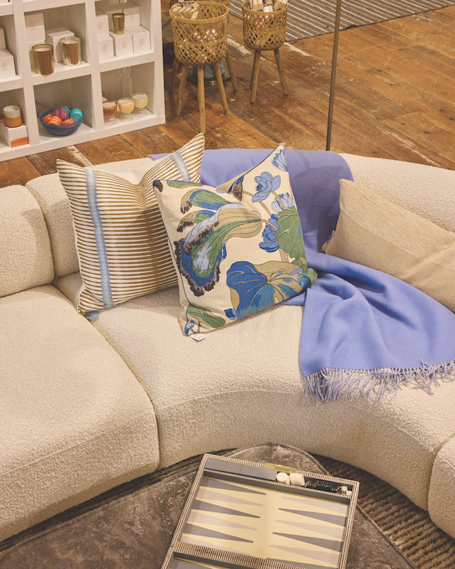Curved cream sofa with colorful patterned pillows, blue throw and decorative tray