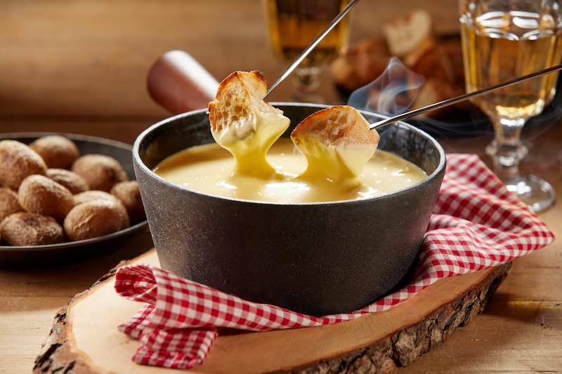 Pieces of bread dipped into melted cheese in a fondue pot.