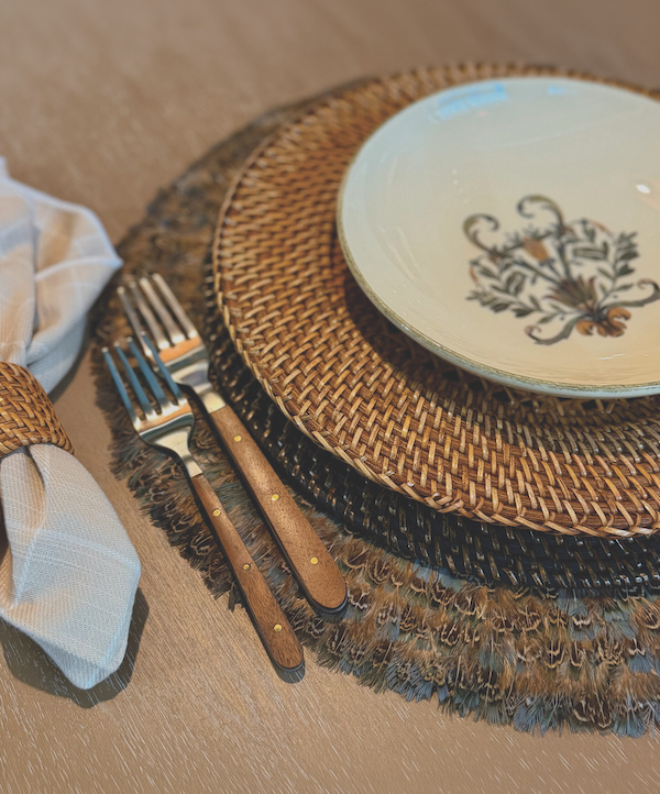 Patterned dinner plate on a woven charger with wood-handled flatware and folded napkin