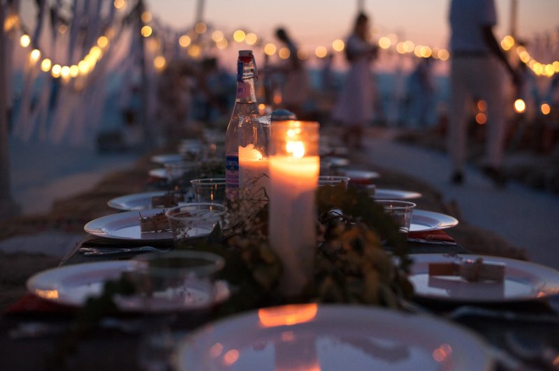 Candlelit outdoor dining table with string lights in the background