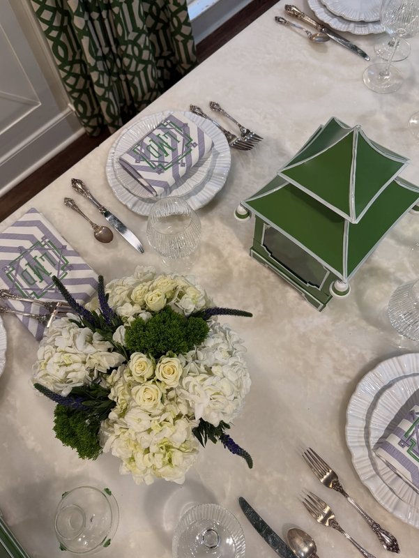 Overhead view of a table with white flowers, patterned plates, folded green napkins and silverware
