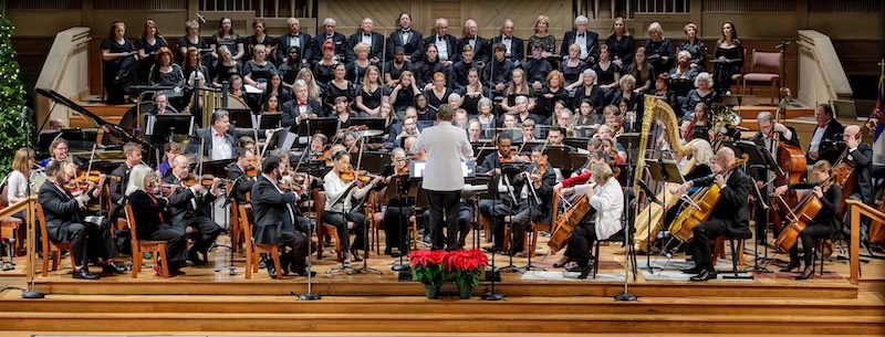 Full symphony orchestra and chorus perform together on a concert stage.