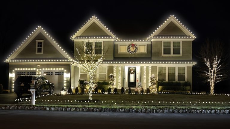 Lowcountry home decorated with warm white Christmas lights along the roofline, trees and front entrance.